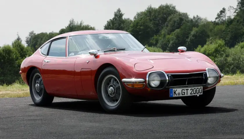 Klasyczny, czerwony Toyota 2000GT, jeden z najbardziej pożądanych japońskich samochodów sportowych, prezentuje swoje eleganckie linie na tle zieleni.
