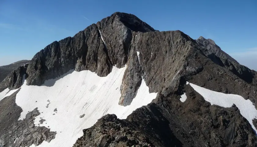 Cumbre rocosa y nevada de un pico posets bajo un cielo azul despejado.