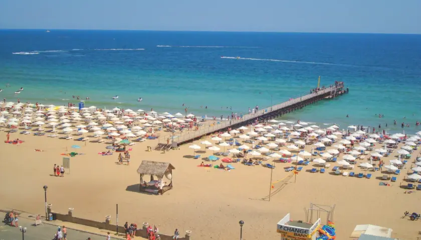Słoneczny Brzeg, Bułgaria: plaża pełna białych parasoli, molo i turystów cieszących się słońcem i morzem.