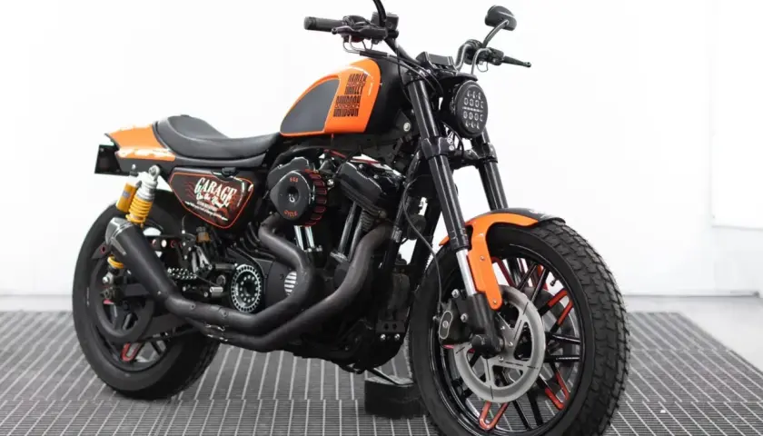 Harley Davidson custom con sella nera, serbatoio arancione e dettagli "Garage". Motore potente e ruote personalizzate.