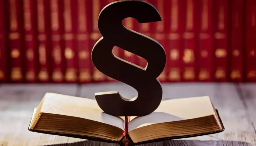 Symbol paragrafu na otwartej księdze, w tle rząd czerwonych ksiąg. Symbolizuje prawo i sprawiedliwość, a może nawet nadzieję na amnestia.