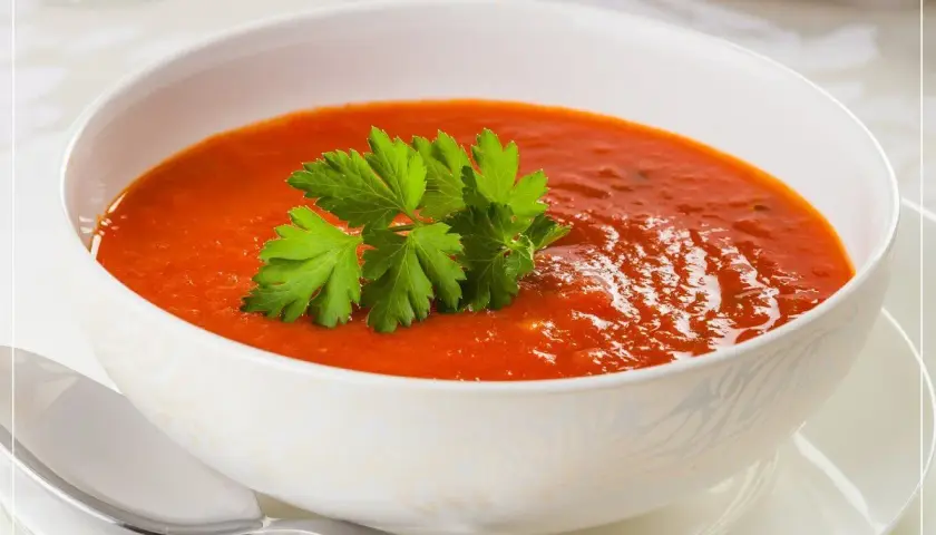 Eine Schüssel cremiger Tomatensuppe mit Petersilie garniert, daneben ein Löffel.