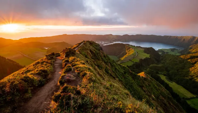 Magnifique paysage des Açores au coucher du soleil, avec un sentier serpentant sur une crête verdoyante menant à un lac paisible.
