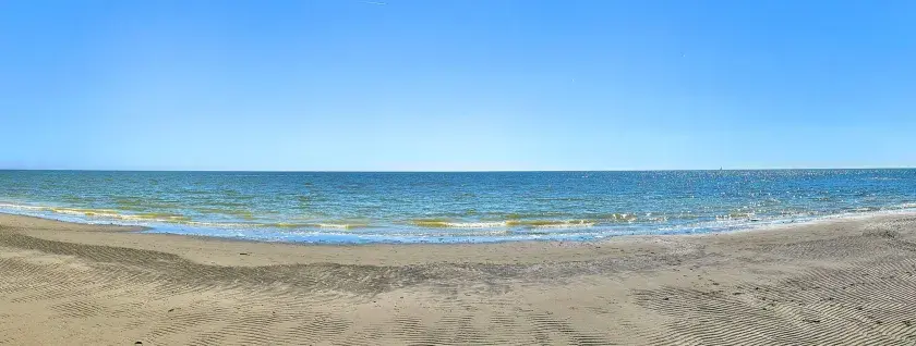 Vaste étendue de sable et de mer au Lido degli Estensi sous un ciel bleu clair. Des vagues douces caressent le rivage.