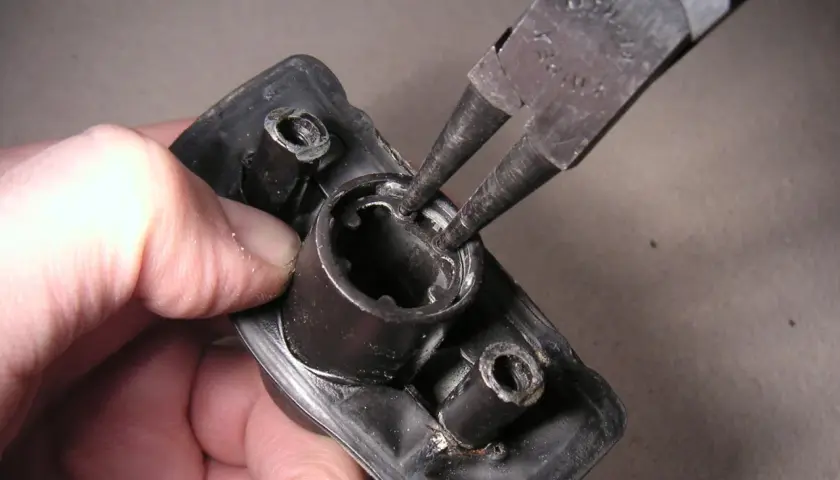 Mit einer Seegeringzange wird ein Sicherungsring aus einem schwarzen Bauteil entfernt.