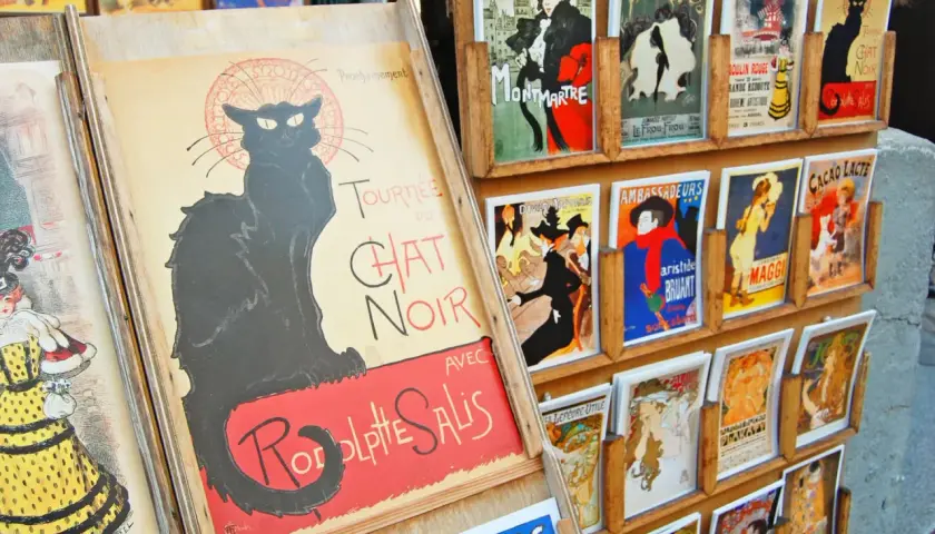Affiches de chat art, dont une grande affiche du Chat Noir, exposées sur un présentoir en bois.