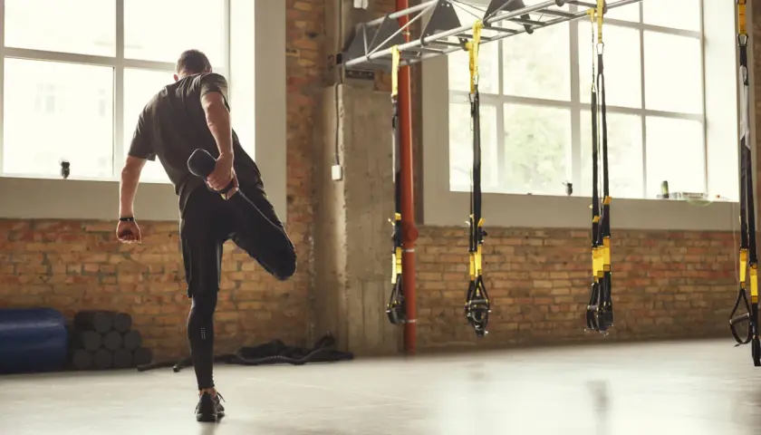 Hombre estirando la pierna, un ejemplo de la definición de calentamiento en un gimnasio con ladrillos y TRX.