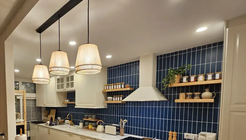 Una lámpara negra y madera ilumina esta cocina moderna con azulejos azules y encimeras de mármol.
