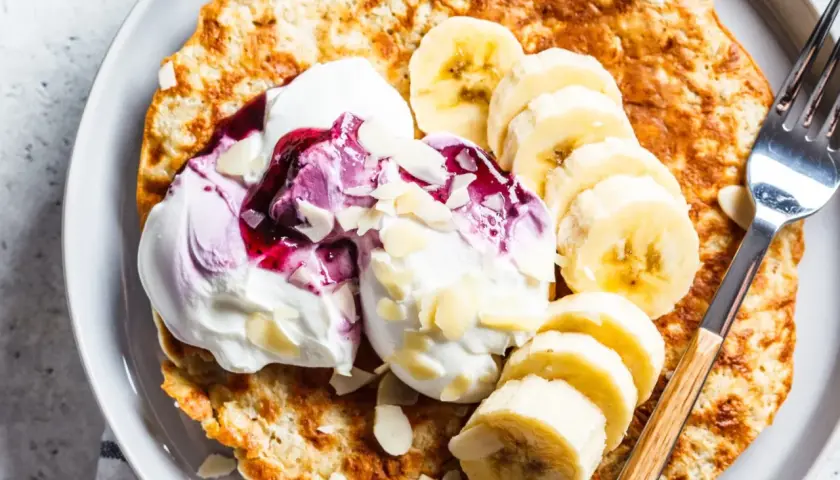 Puszysty omlet bananowy z jogurtem, musem jagodowym i płatkami migdałów na talerzu.