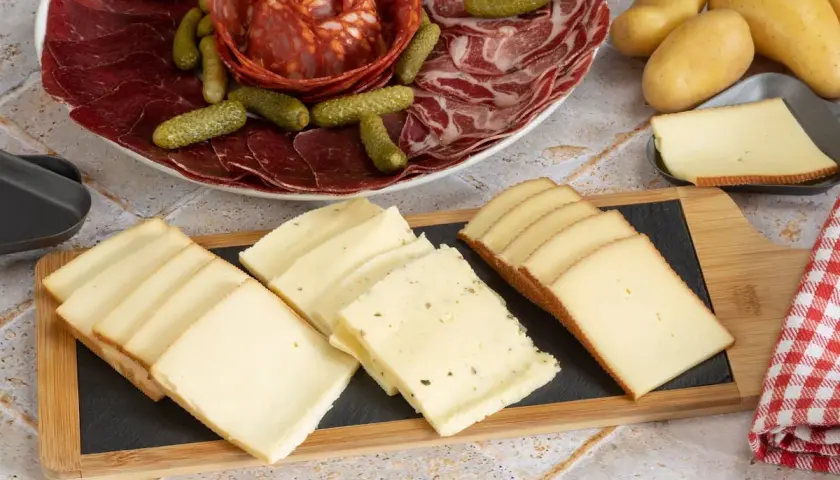 Plateau de charcuterie et fromages variés, prêts pour une recette fromage à raclette. Pommes de terre et cornichons complètent ce festin.