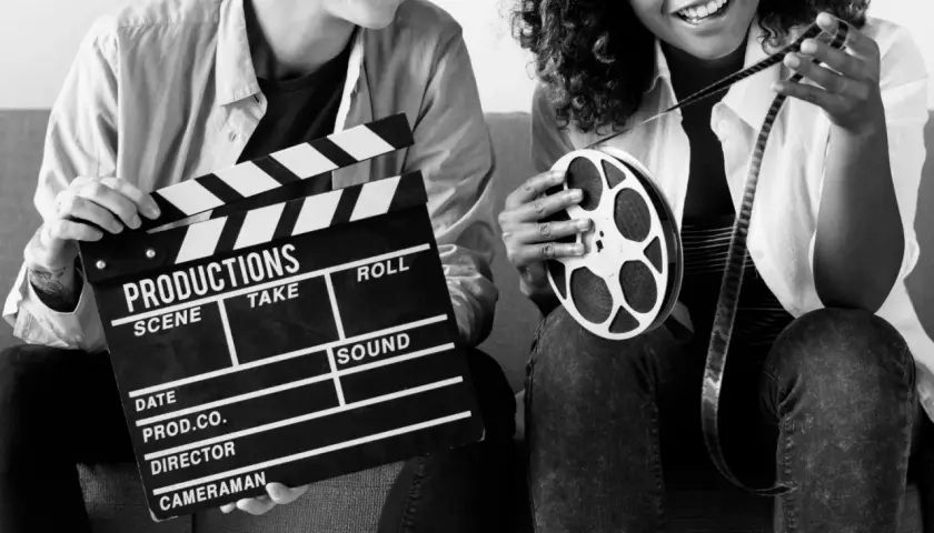 Dwie osoby z klapsem filmowym i rolką taśmy filmowej. Zastanawiasz się, ile zarabia reżyser filmowy?