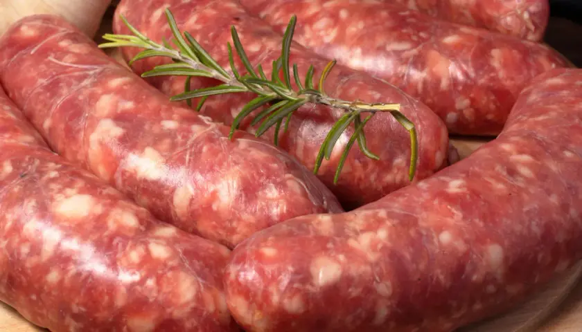 Surowe kiełbaski, czyli salsiccia, z gałązką rozmarynu i czosnkiem. Idealne do grillowania.