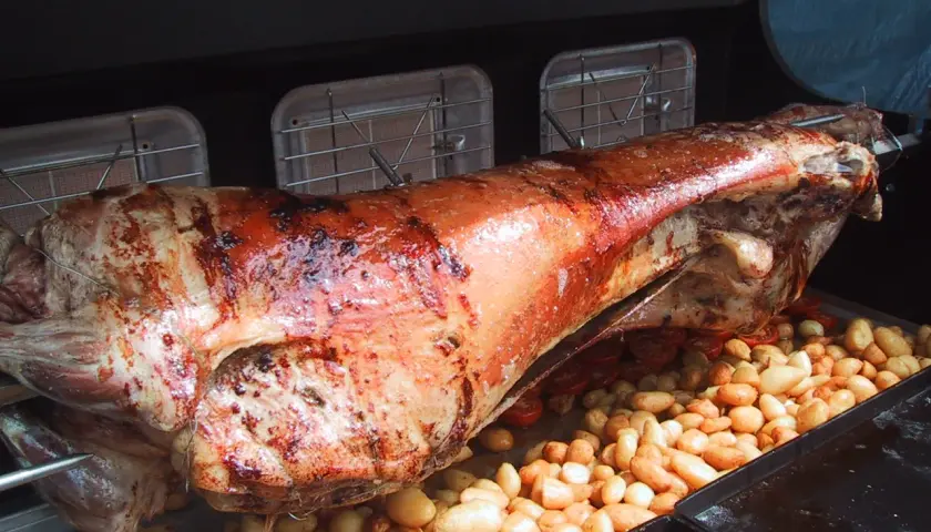 Gigot à la broche doré et juteux, rôti lentement avec des pommes de terre et des tomates cerises en dessous.