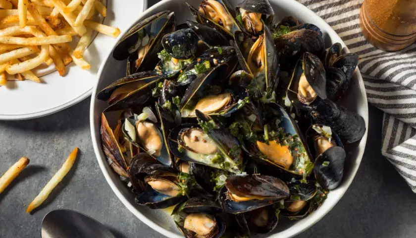 Un plat généreux de moules au feu de bois, parsemées d'herbes fraîches et servies avec des frites croustillantes.