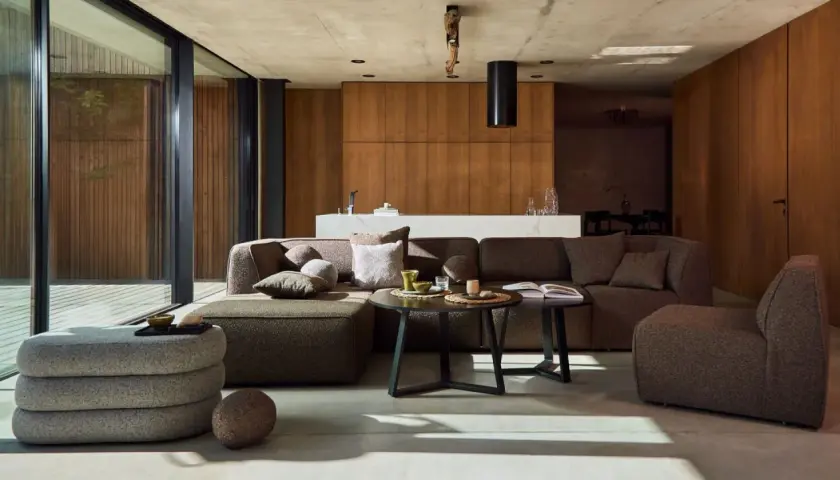 Nowoczesny salon w stylu bauhaus z dużą, narożną sofą, drewnianymi panelami i betonowym sufitem.