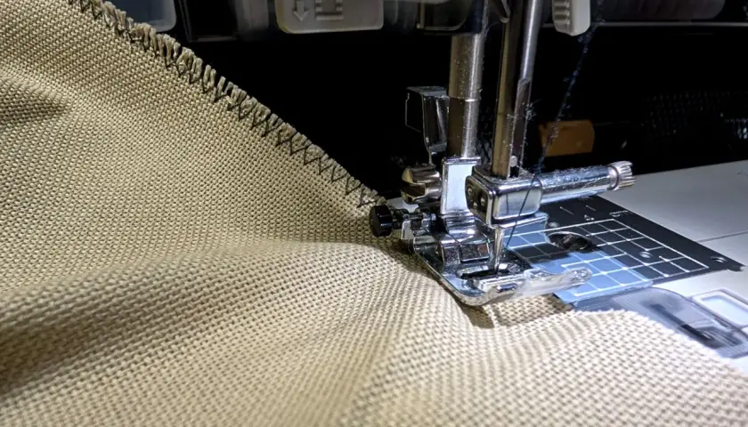 Sewing a zigzag stitch on a tan fabric to prevent fraying. This technique helps keep edges neat, unlike how some flannel might fray.