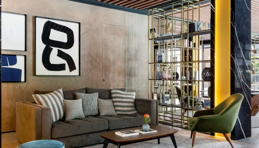 Sofá gris con cojines decorativos, mesa de centro y estantería dorada en un lobby de Radisson Collection.