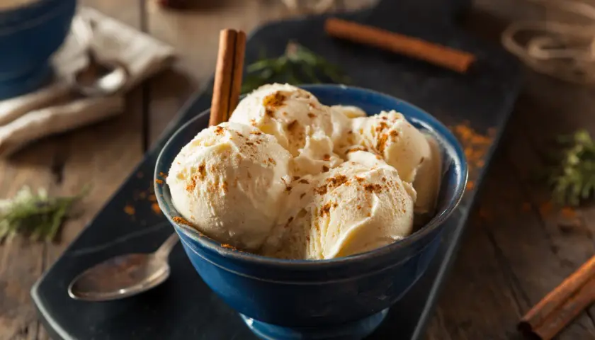 Pyszne lody zabajone w niebieskiej miseczce, posypane cynamonem i ozdobione laską cynamonu.