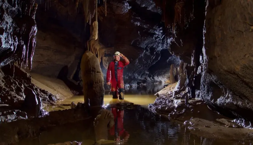 Eksplorator w jaskini, zanurzony po kolana w wodzie, odkrywa tajemnice speleologii.