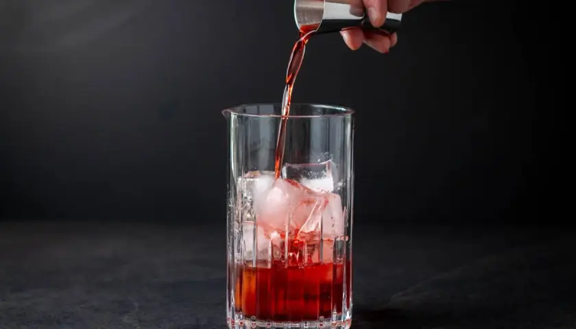 Ein Barkeeper gießt rote Flüssigkeit in ein Glas mit Eiswürfeln. Der klassische Cocktail Negroni nimmt Gestalt an.