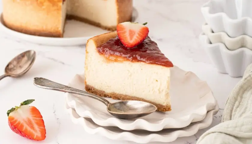 Deliciosa tarta de queso vegana con cobertura de fresa y una fresa fresca encima.