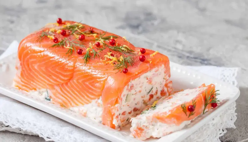 Une délicieuse terrine de saumon, garnie d'aneth, de baies roses et de zeste de citron, prête à être dégustée.