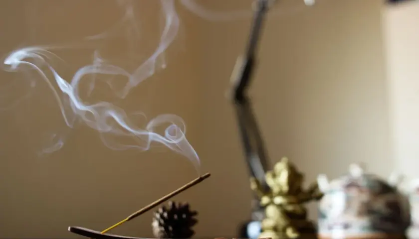 El humo del incienso se eleva en espirales blancas, creando un ambiente sereno junto a una figura dorada y una tetera decorada.