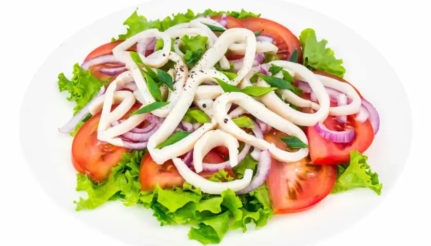 Deliziosa insalata di calamari con pomodori, cipolla rossa e lattuga fresca, condita con erbe aromatiche.