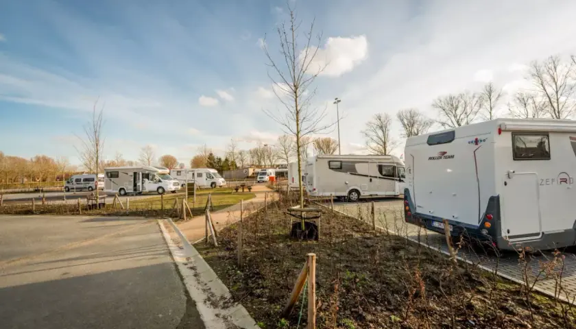 Vue d'une aire camping car Bruges avec plusieurs véhicules stationnés sous un ciel bleu.