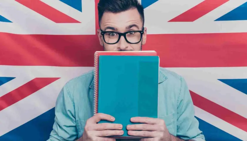 Studente con quaderni davanti al volto, sullo sfondo la Union Jack. Chissà se impara come si dice "venerdì" in inglese.