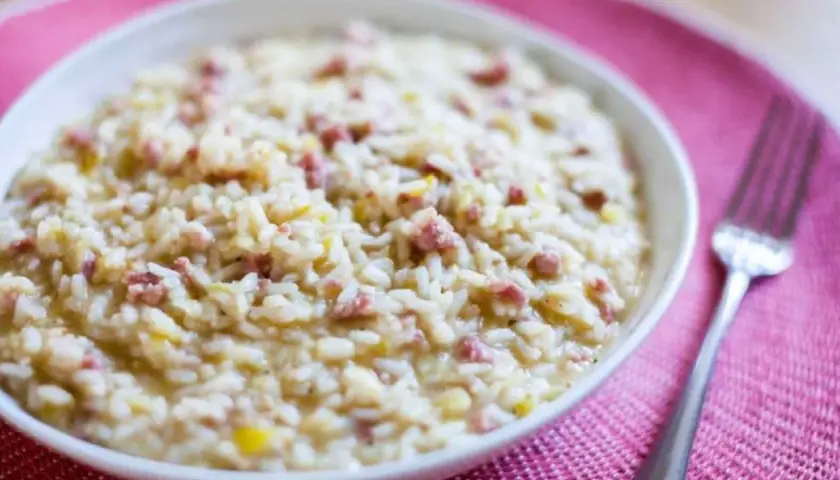 Un cremoso risotto salsiccia, con trocitos de salchicha italiana, servido en un cuenco blanco sobre un mantel rosa.