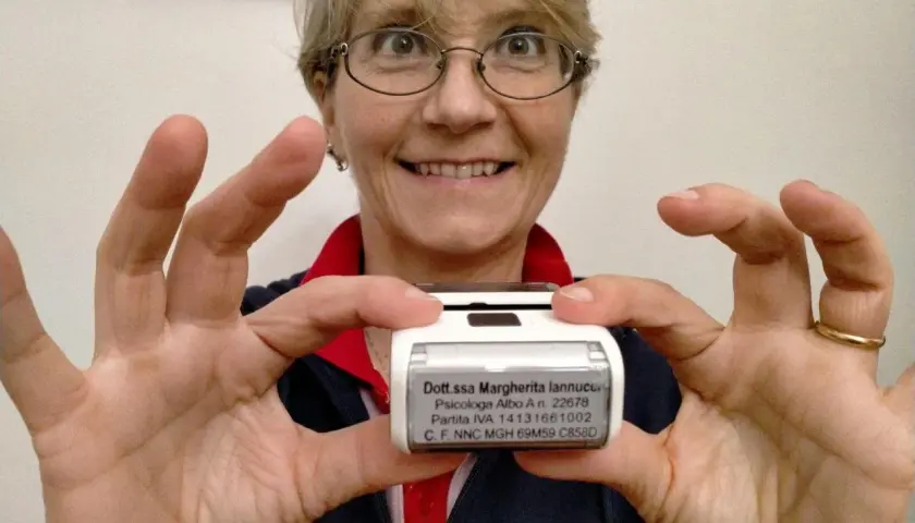 Donna sorridente mostra un timbro con i dati di una psicologa. Utile per sapere cosa scrivere su un timbro psicologo.
