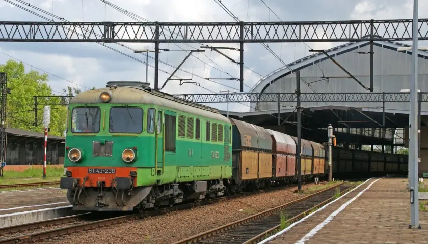 Zielona lokomotywa ST43-238 z wagonami towarowymi na torach kolejowych, pod zadaszeniem dworca.
