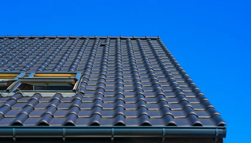 Toit en tuiles sombres, avec deux fenêtres de toit ouvertes, sous un ciel bleu vif. Ces matériaux de couverture sont bien posés.