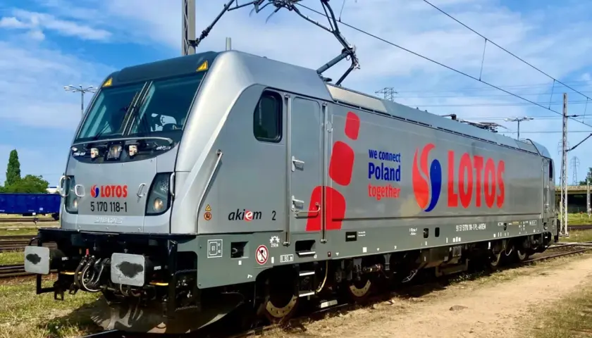 Srebrna lokomotywa Traxx z napisem LOTOS i hasłem "we connect Poland together" stoi na torach.