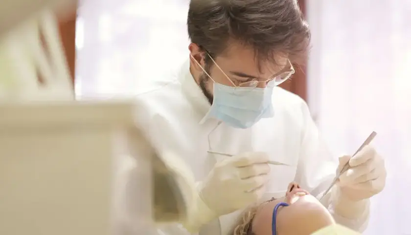 Dentysta w masce i rękawiczkach wykonuje zabieg. Pacjentka leży na fotelu. Pytanie o ile l4 po wyrwaniu ósemki.