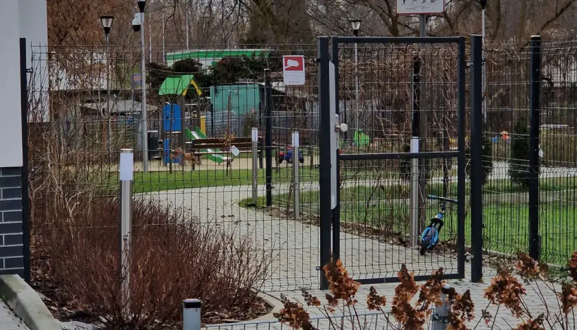 Prawda o ustawie która ma zakazać grodzenia osiedli w dużych miastach: ogrodzony plac zabaw z bramą i tablicą informacyjną.