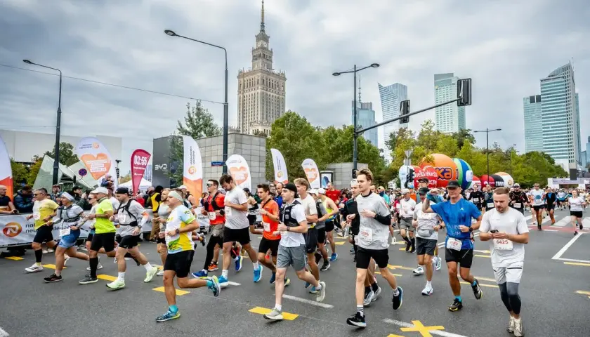 Uczestnicy maratonu biegną ulicą na tle Pałacu Kultury i Nauki.