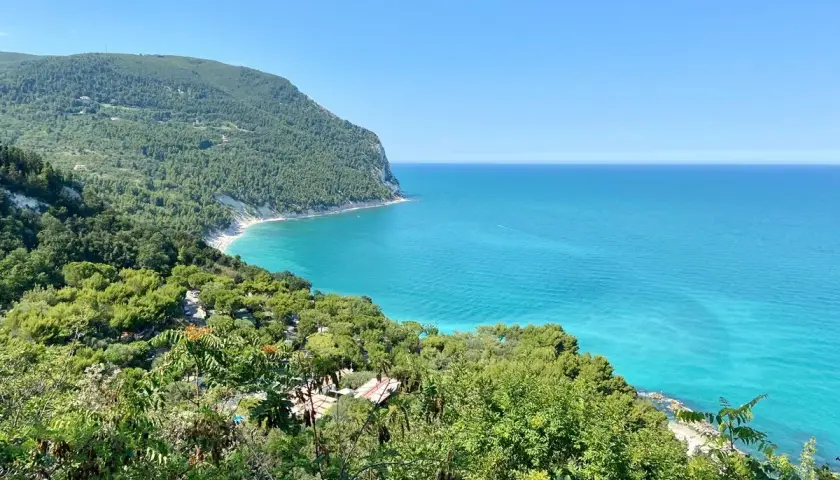 Vista mozzafiato sulla costa marchigiana, un gioiello tra le 10 cose da vedere nelle Marche. Mare turchese e verde lussureggiante.