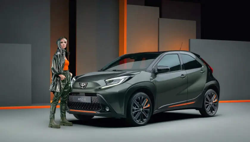Stylowa kobieta obok zielonego Toyota Aygo X. Wiele osób szuka pozytywnych toyota aygo opinie, ten model wygląda obiecująco.