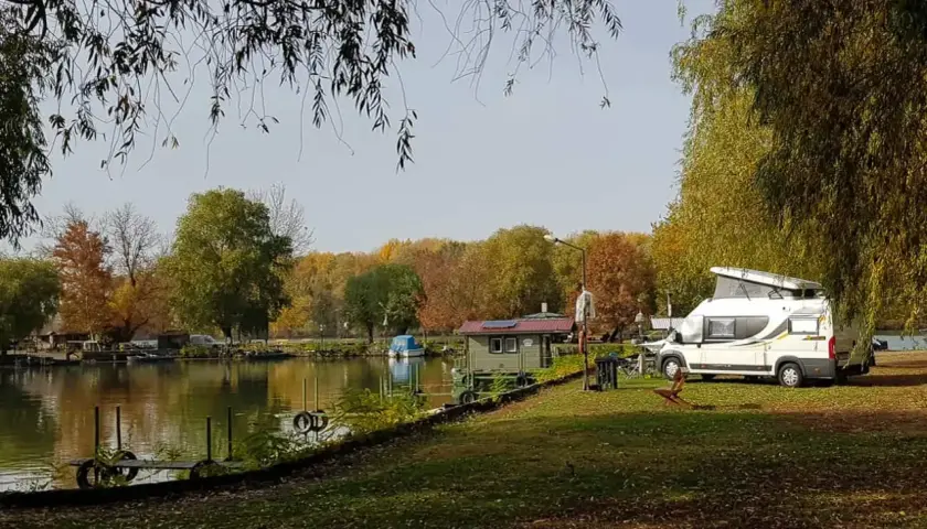Jesień na Węgrzech. Kamper zaparkowany nad jeziorem, w tle kolorowe drzewa i mała chatka.