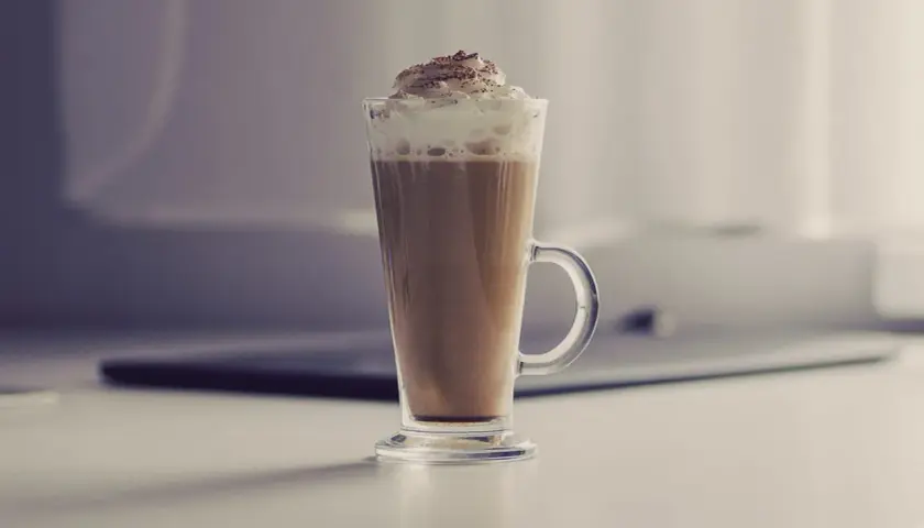 Jak zrobić latte macchiato? Wysoka szklanka z kawą, mlekiem i bitą śmietaną, posypana kakao. Idealny napój na chłodne dni.
