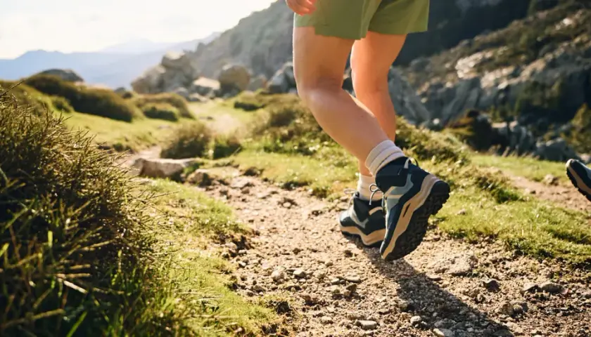 Hiking boots, one leather, one synthetic, tread a rocky path through a sun-drenched mountain landscape.