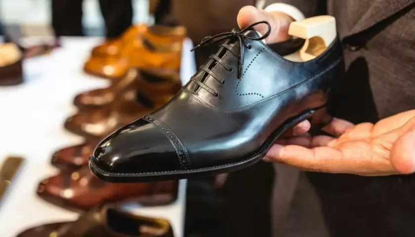 Main d'un homme tenant une chaussure noire brillante, prête à nourrir le cuir. D'autres chaussures en cuir sont alignées en arrière-plan.