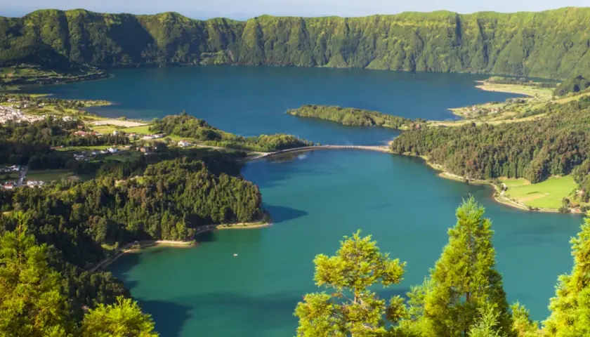 Malowniczy krajobraz portugalskiego archipelagu na Atlantyku: jezioro w kraterze wulkanicznym, otoczone zielonymi wzgórzami i niewielką wioską.