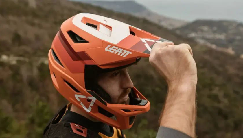 Uomo con casco integrale Leatt arancione, pronto per downhill. Il casco integrale significato è protezione totale.
