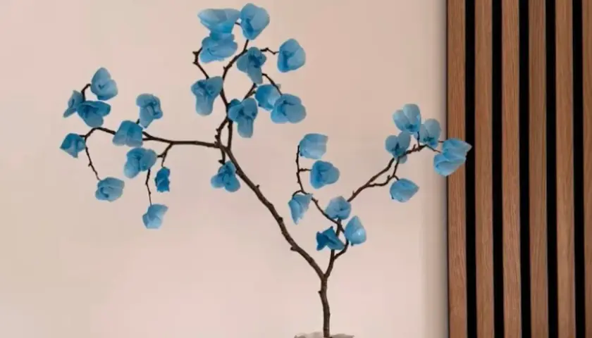 Une branche décorative avec des fleurs bleues en papier, une composition florale à faire soi-même.