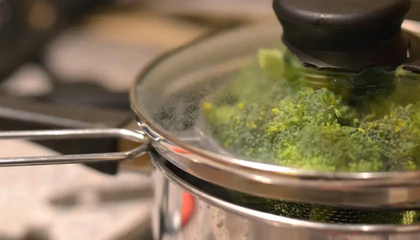 Grön broccoli ångas i en kastrull med glaslock. Snart redo att serveras!