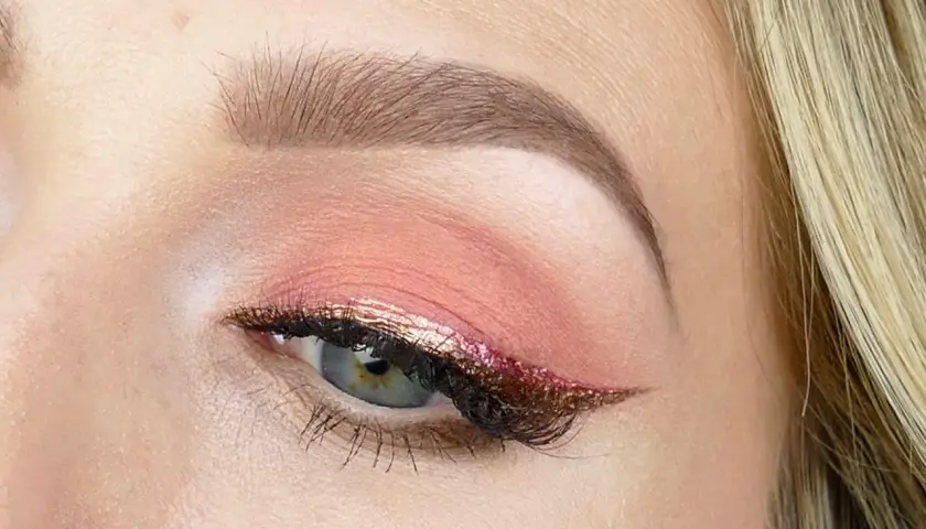 En närbild på ett öga med en vacker rosa sminkning. Ögonlocket har en mjuk rosa skugga och en glittrig eyeliner i guld och rosa.