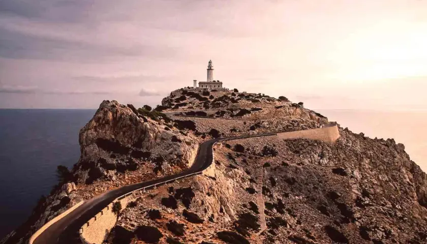 Faro en la cima de un acantilado rocoso, con una carretera serpenteante que asciende. Un paisaje de monumentos naturales impresionantes.